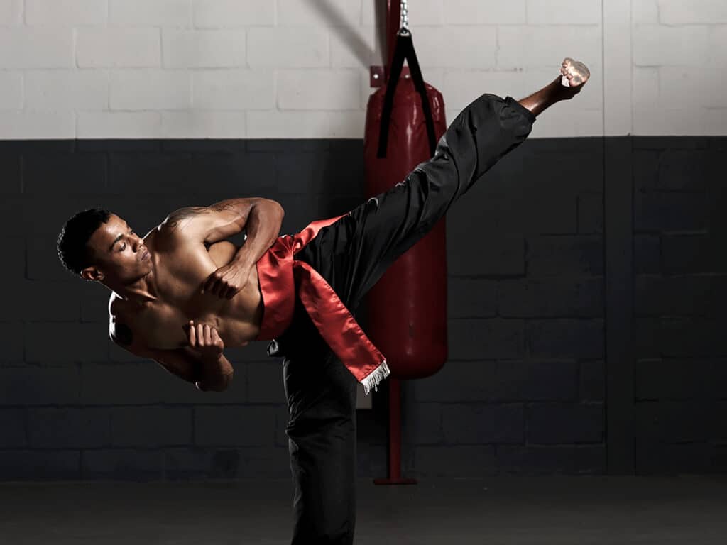 A martial artist with black pants kicking a leg out far in front of him.